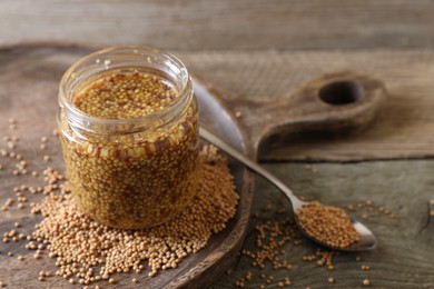 Photo of Jar and spoon of whole grain mustard on wooden table. Space for text
