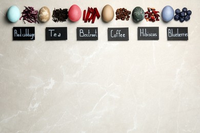 Photo of Easter eggs painted with natural organic dyes and labels on light grey table, flat lay. Red cabbage, tea, beetroot, coffee beans, hibiscus, blueberries used for coloring. Space for text