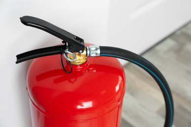 Fire extinguisher near white wall indoors, closeup 