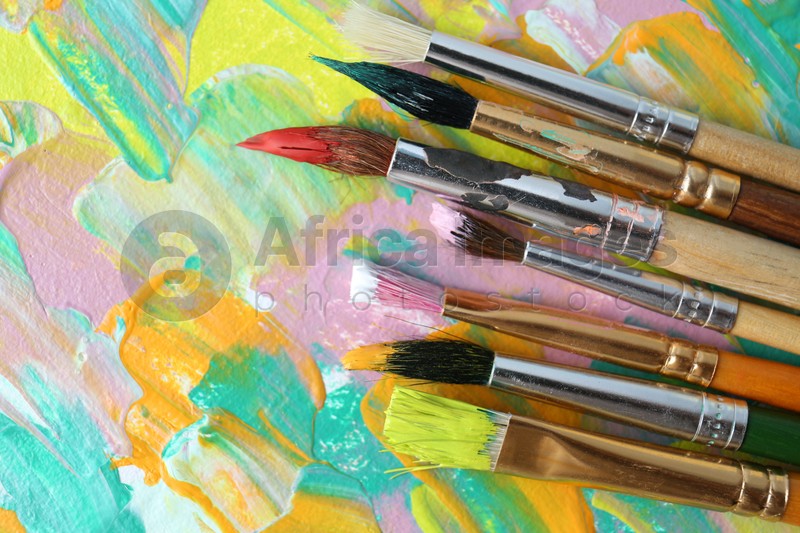 Set of different brushes on abstract colorful paint, flat lay