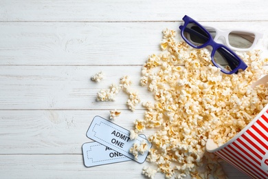 Bucket of fresh popcorn, tickets and 3D glasses on white wooden table, flat lay with space for text. Cinema snack