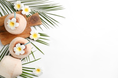Fresh coconuts with drinking straws and flowers on white background, flat lay. Space for text