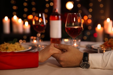 Couple holding hands together at table during romantic dinner in restaurant, closeup
