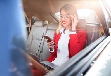 Young businesswoman with smartphone and laptop in car