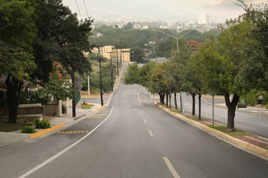 Beautiful city street with wide asphalt road and green trees