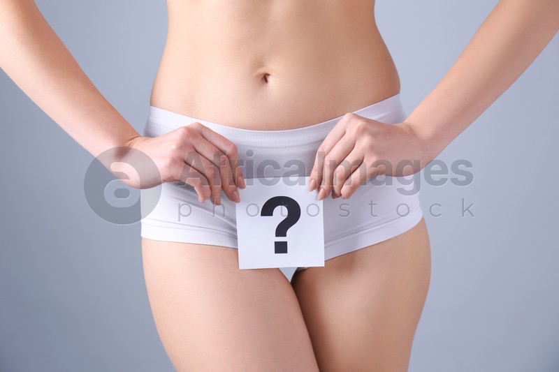 Young woman holding paper with question mark near underwear on grey background. Gynecology