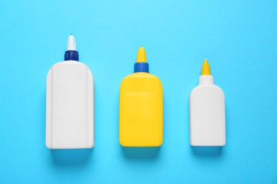 Different bottles of glues on light blue background, flat lay
