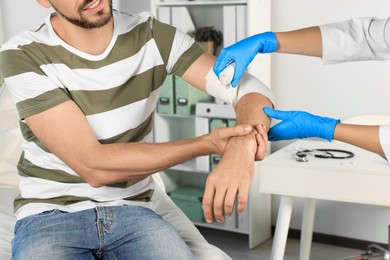 Doctor applying bandage onto patient's arm at hospital, closeup