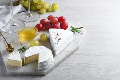 Tasty brie cheese with honey, rosemary and grapes on white wooden table, space for text
