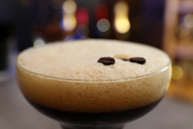 Glass of Espresso Martini with coffee beans on blurred background, closeup. Alcohol cocktail