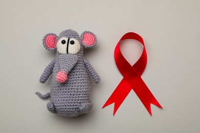 Photo of Cute knitted toy mouse and red ribbon on beige background, flat lay. AIDS disease awareness