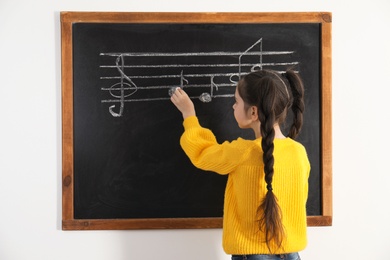Little girl writing music notes on blackboard in classroom