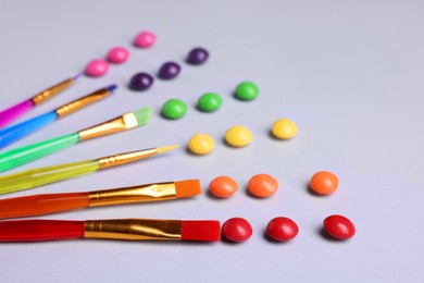 Creative composition with paint brushes and colorful candies on light grey background, closeup