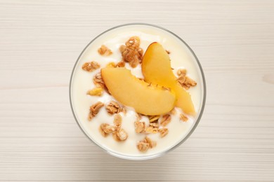 Photo of Tasty peach yogurt with granola and pieces of fruit in dessert bowl on white wooden table, top view