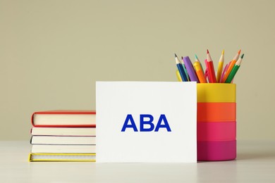 Photo of Set of stationery and card with abbreviation ABA (Applied Behavior Analysis) on wooden table against beige background