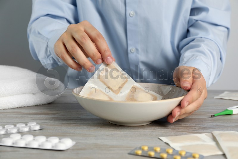 Woman dipping mustard plaster into bowl with water at wooden table, closeup