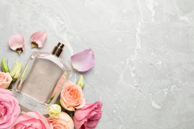 Flat lay composition with bottle of perfume and fresh flowers on light grey marble background, space for text