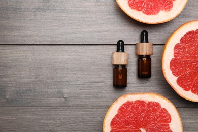 Bottles of citrus essential oil and grapefruit slices on wooden table, flat lay. Space for text