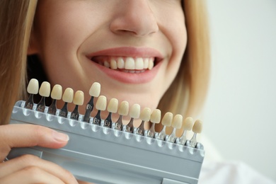 Woman matching teeth color with palette on white background, closeup. Cosmetic dentistry