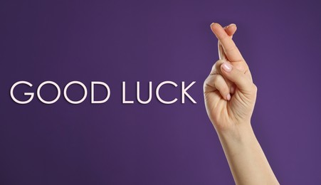 Woman with crossed fingers on violet background, closeup. Good luck superstition