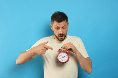 Emotional man with alarm clock on light blue background. Being late concept