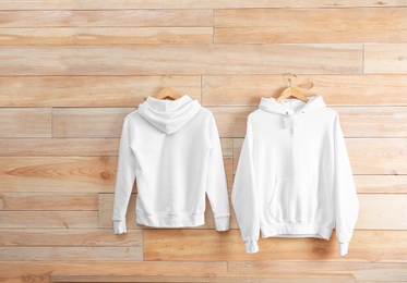 New hoodie sweaters with hangers on wooden wall. Mockup for design