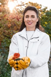 Photo of Woman in gardening gloves holding pile of soil with flowers outdoors