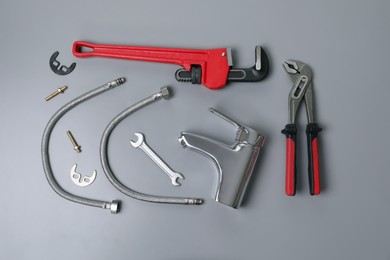 Parts of water tap and wrenches on grey background, flat lay
