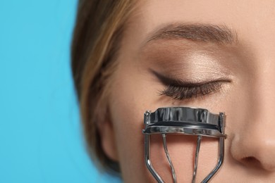 Young woman with eyelash curler on light blue background, closeup