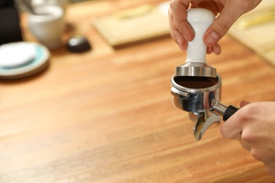Barista tamping milled coffee in portafilter at bar counter, closeup. Space for text