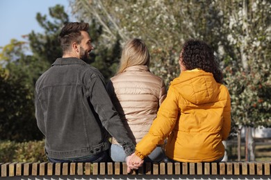 Man holding hands with another woman behind his girlfriend's back on bench in park. Love triangle