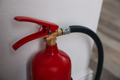 Fire extinguisher near white wall indoors, closeup