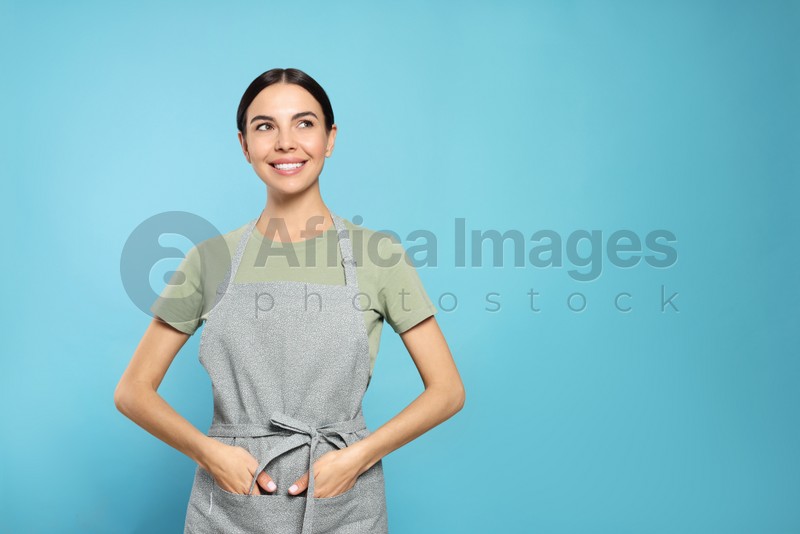 Young woman in grey apron on light blue background, space for text