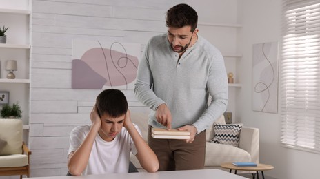 Strict father with books scolding his son at home. Teenager problems