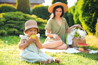 Mother and her daughter having picnic in garden, focus on baby with apple