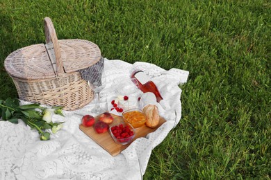 Picnic blanket with tasty food, flowers, basket and cider on green grass outdoors. Space for text