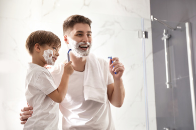 Dad and son with shaving foam on their faces having fun in bathroom