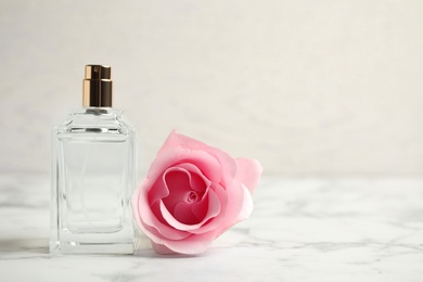 Bottle of perfume and beautiful rose on white marble table. Space for text