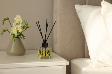 Aromatic reed air freshener and freesia flowers on white bedside table in bedroom