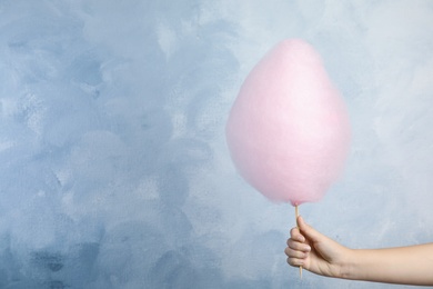 Photo of Woman holding sweet pink cotton candy on light blue background, closeup view. Space for text