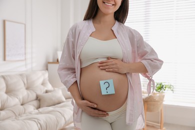 Pregnant woman with sticky note on belly at home, closeup. Choosing baby name