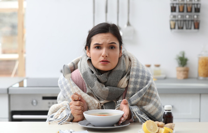 Sick young woman eating soup to cure flu at table in kitchen