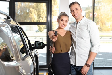 Young couple with key near new car in dealership