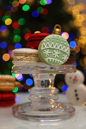 Photo of Beautifully decorated Christmas macarons on white table against blurred festive lights