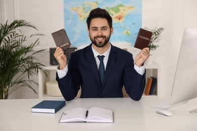 Happy manager holding passports at desk in travel agency