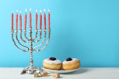 Silver menorah, dreidels with He, Pe, Nun, Gimel letters and sufganiyot on white table, space for text. Hanukkah symbols