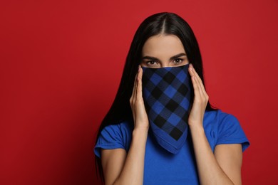 Young woman with bandana covering her face on red background, space for text