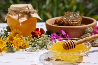 Delicious honey, combs and different flowers on white wooden table in garden. Space for text