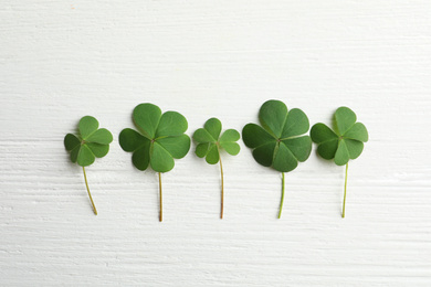 Clover leaves on white wooden table, flat lay. St. Patrick's Day symbol