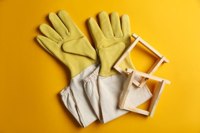 Beekeeping gloves and honeycomb frames on yellow background, flat lay